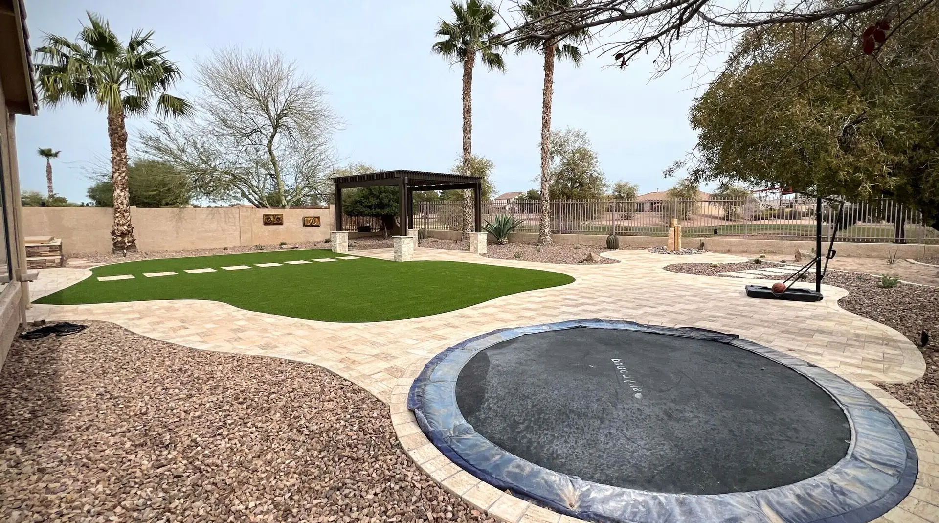 Backyard remodel featuring travertine patio, artificial turf, shaded pergola, and fire pit, designed for family gatherings and outdoor enjoyment in Chandler, AZ.