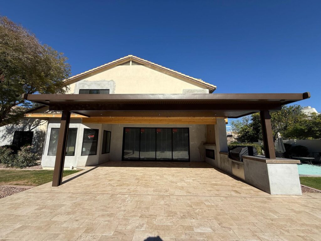 Backyard remodel in Chandler, AZ featuring a spacious travertine patio, a modern pergola providing shade, and a cozy fireplace, designed for family gatherings and outdoor enjoyment.