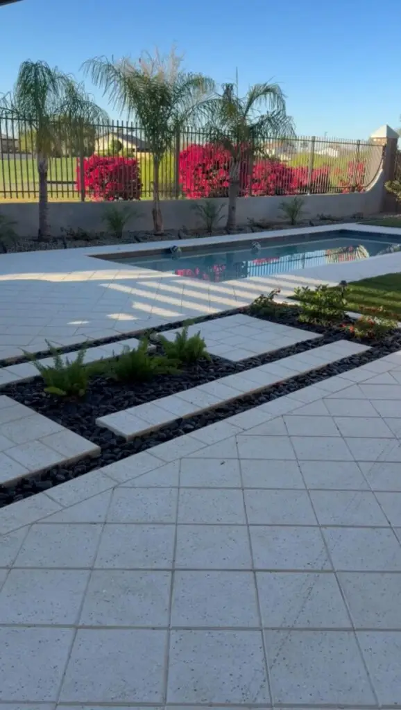 Backyard remodel in Gilbert, AZ featuring a modern pool, landscaped patio with geometric pavers, vibrant green plants, and a backdrop of blooming bougainvillea under clear blue skies.