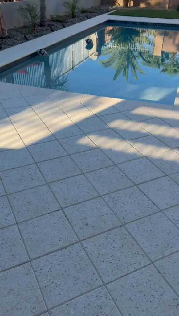 Modern pool area with clear water, surrounded by textured tiles and palm trees, showcasing a transformed backyard in Gilbert, AZ.