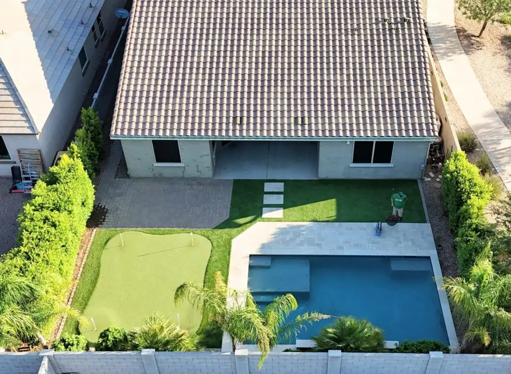 Backyard remodel in Queen Creek, AZ featuring artificial turf, putting green, travertine pavers, and a swimming pool, showcasing a vibrant outdoor space designed for relaxation and entertainment.