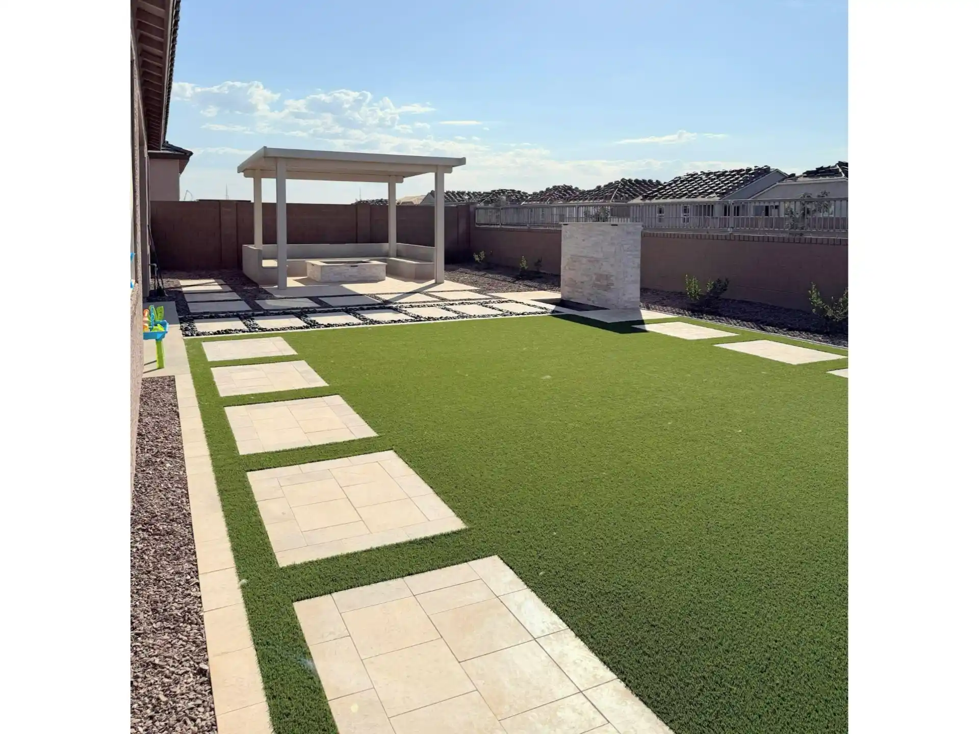 Backyard remodel featuring artificial grass, stone pavers, and a modern pergola in a residential setting, showcasing a transformed outdoor space for relaxation and entertainment.