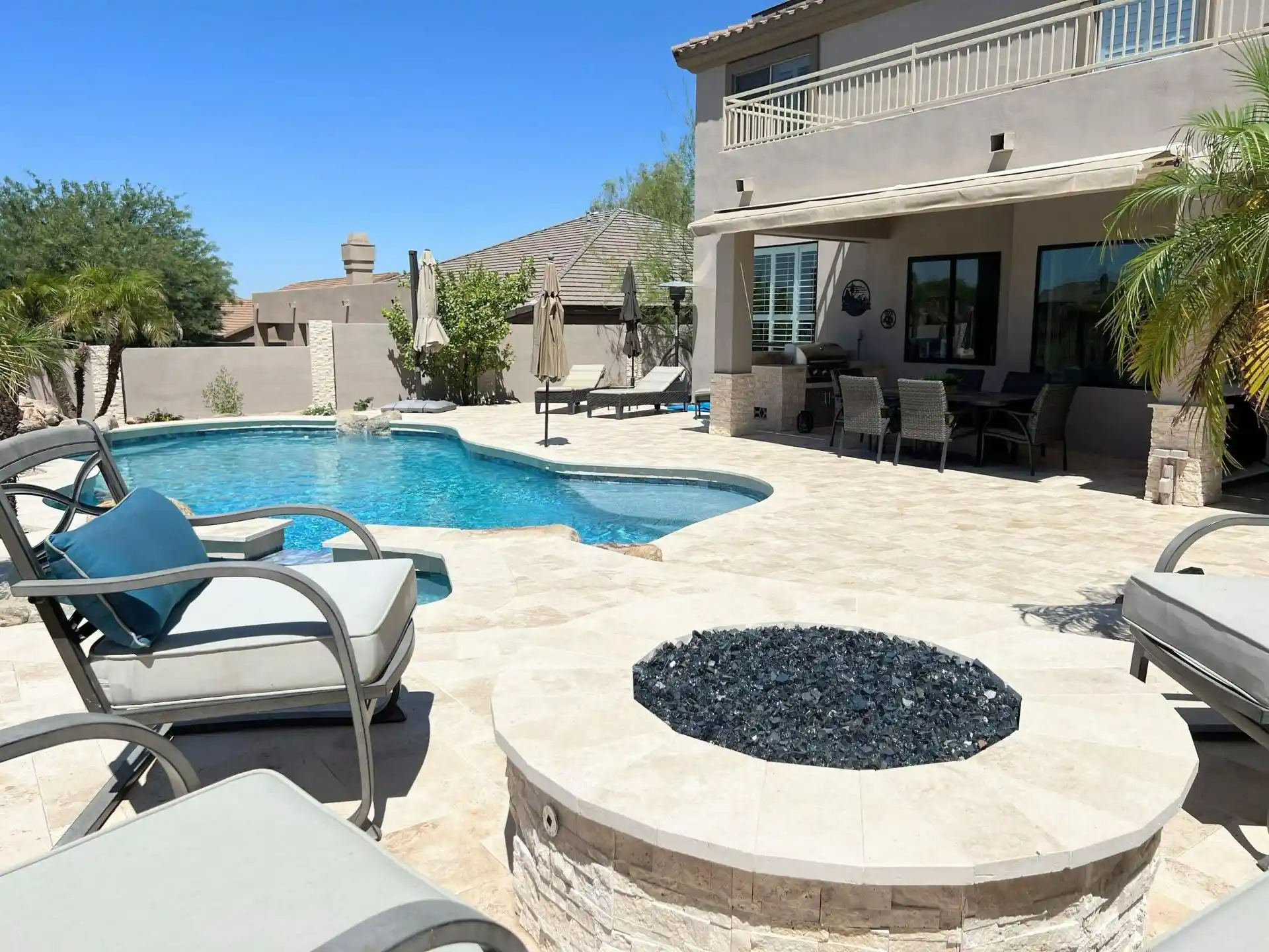 Backyard remodel featuring a modern pool, lounge chairs with blue cushions, and a fire pit, showcasing a transformed outdoor space for relaxation and entertainment in Gilbert, AZ.