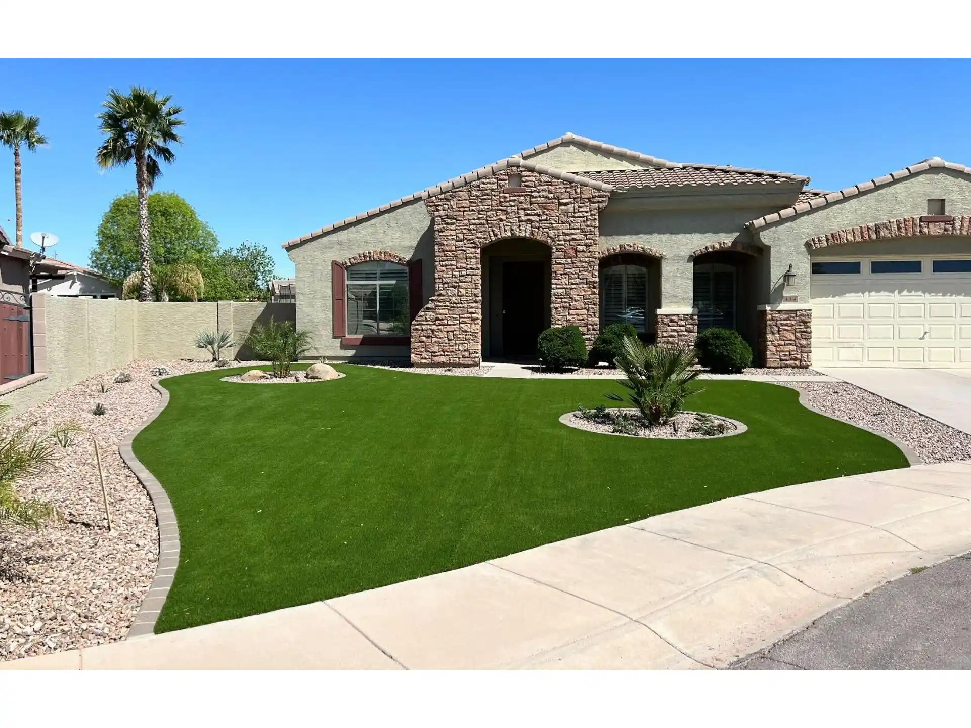 Front yard remodel featuring lush green artificial grass, decorative rocks, and modern landscaping elements, enhancing the home's curb appeal in a residential setting.