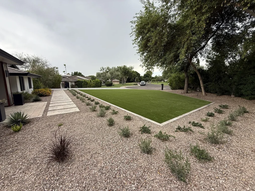 Artificial turf lawn in Phoenix, AZ edged with a travertine border, surrounded by decorative granite and new desert shrubs