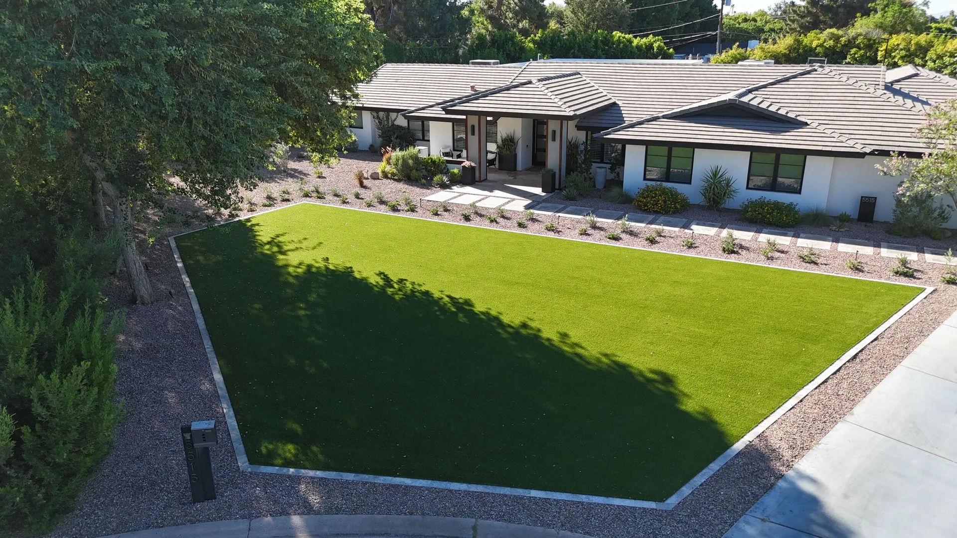 Aerial view of a finished front yard remodel in Phoenix, AZ with an artificial turf lawn, travertine border, decorative granite and new desert plantings