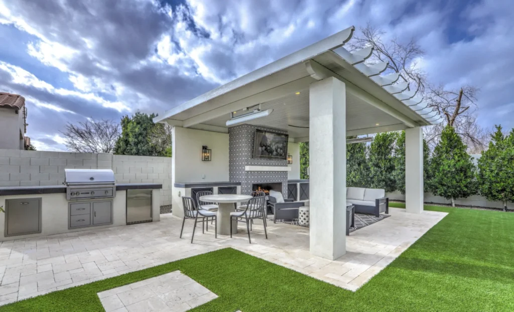 Outdoor kitchen island with built-in grill and storage in a Chandler, AZ backyard beside a ramada and artificial turf lawn