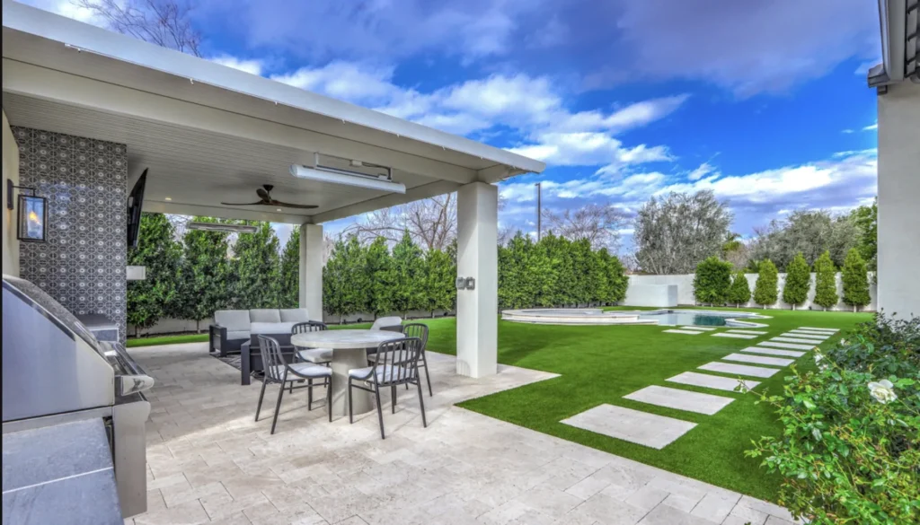 Built-in stainless outdoor kitchen under a ramada in Chandler, AZ with a remodeled pool and artificial turf lawn beyond