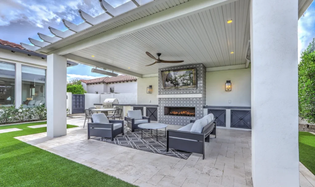 Chandler, AZ outdoor living space with a ramada, gas fireplace, travertine paver patio and built-in outdoor kitchen in the background