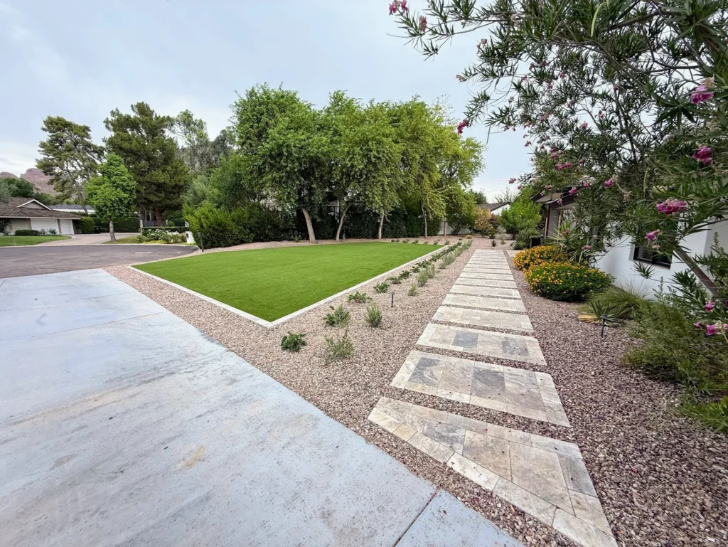 Travertine paver walkway through a Phoenix, AZ front yard with flowering shrubs, decorative granite and artificial turf